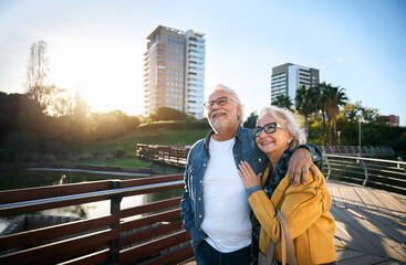 Senior couple walking arm in arm, smiling at sunset in a city park, enjoying a romantic and...