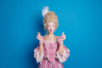 Elegant woman in baroque costume posing against a vibrant blue backdrop, showcasing historical...