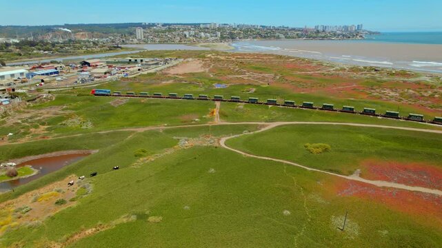 Aerial view following a cargo train passing over Ritoque in Quintero in Chile