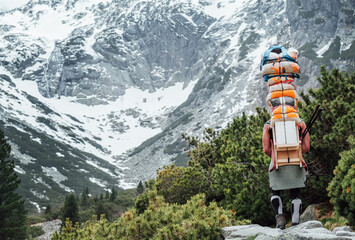 Strong man working as porter carrying huge cargo with traditional method for High Tatry region for altitude Mountain huts cargo provision delivery. Nature, transportation or goods delivery concept.