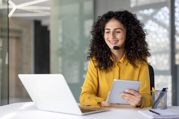 Woman with headset at workplace inside office holding tablet computer. Office worker of customer...
