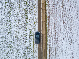 This aerial image captures a car navigating along a snowcovered road, which is flanked by open fields