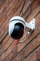A camera part of a home security system is mounted on a brick wall. The camera is pan-tilt,...
