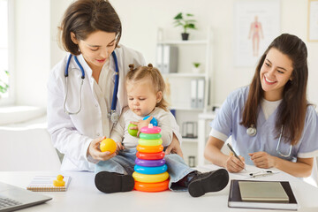 Fototapeta premium Pediatrician doctor and nurse playing with a young girl patient using toys during a hospital appointment. Promoting support and creating a comfortable environment during a medical visit.