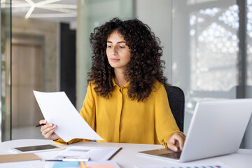 Serious thinking woman holds a document in her hands, reads and checks statistical indicators....