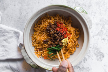 Spicy instant noodles with slices of red chili ginger scallions minced pork, spicy ramen noodles in a donabe clay pot
