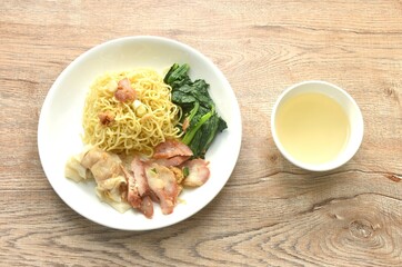 dry Chinese egg yellow noodles with red barbecue pork and dumpling in on plate with clear soup cup