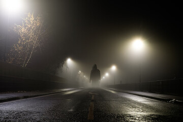 A creepy transparent  hooded ghost, standing in the middle of the road on a spooky foggy night