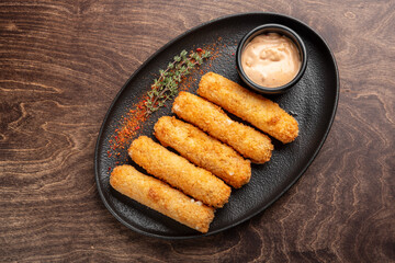 Crispy golden cheese sticks arranged neatly on a black plate, served with a spicy dipping sauce and...