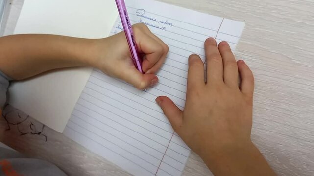 left-handed child writes in a notebook, does homework