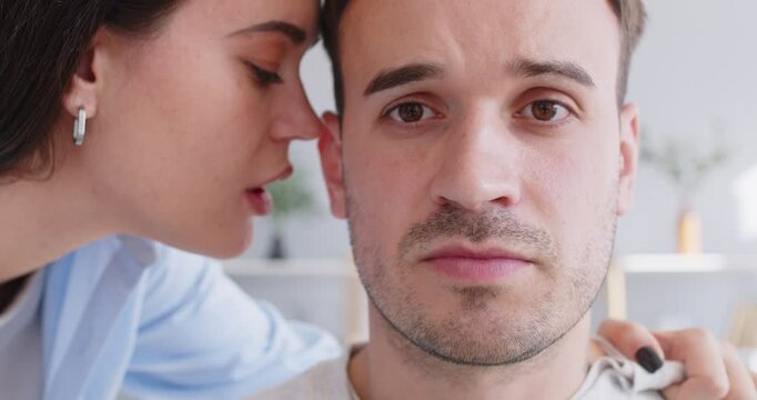 Closeup stressed, serious, unsmiling man listens to angry woman who grabs his shirt, whispers in his ear, tells secret, says something rude and unpleasant, discloses someone's confidential information