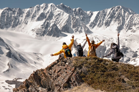 Group of happy friends achieved mountain top, sits and celebrate it at the top with open arms