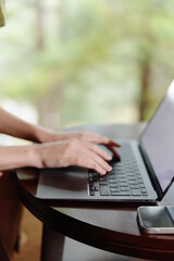 A young woman typing on a laptop at a wooden table in a serene outdoor setting, showcasing a relaxed atmosphere and focus on productivity in nature