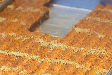 Close-up of golden kunefe dessert topped with crushed pistachios, displayed in a tray, showcasing its intricate shredded pastry texture.