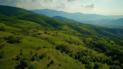 Obraz premium Aerial view of green hills, valley, and distant mountains. Background shows sunny sky, pastoral landscape. Use travel brochure, nature documentary
