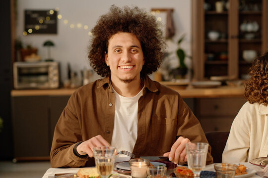Medium close up portrait of curly haired young adult biracial man holding cutlery looking at camera and smiling