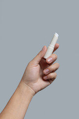 Hand holding white opened lip balm stick against grey close up, cosmetic mockup, copy space