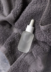 Clear glass dropper bottle with pipette on dark grey bath towel closeup, cosmetic mockup
