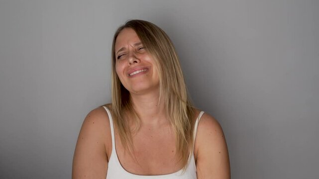 Young whimpering caucasian woman is hysterical, beating the air with her hands on a grey background. Acute emotional reaction, screaming, anger, crying, irritation, nervous attack, drama