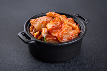 Bowl with korean traditional cabbage kimchi on dark background. Hot fermented napa cabbage.