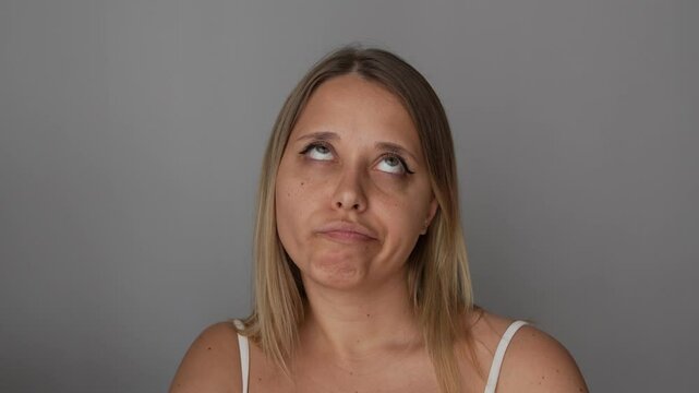 Young displeased blonde woman unhappy about something rolling her eyes on a dark grey color background. Passive aggression, expression of disagreement, irritation, disapproval