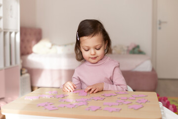 Cute little child girl connecting puzzle pieces on wooden desk in room