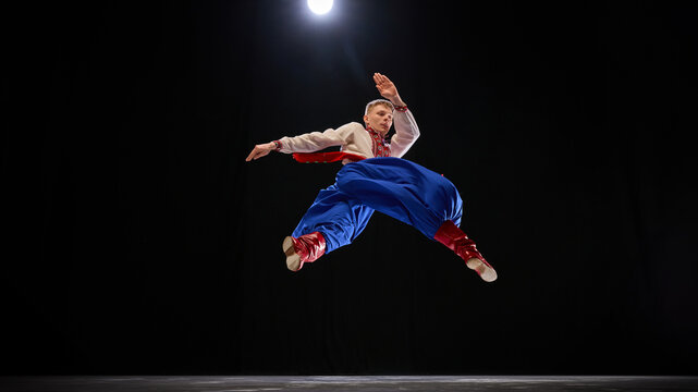 Male dancer flipping mid-air, body twisting with vibrant energy, dressed in traditional attire, representing movement and cultural heritage. Concept of traditions, folk style, people, art and history.