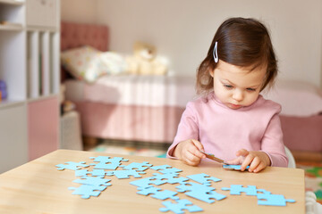 Cute little child girl connecting puzzle pieces on wooden desk in room