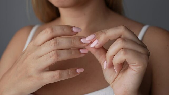 Young woman showing overgrown nail roots on her hands on a dark grey background. Light long nails in pastel colors. Gel nail polish