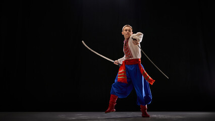 Ukrainian dancer, dancing Hopak with sabre pose, embodying artistry and strength in cultural dance performance against black background. Concept of traditions, folk style, art and history. Ad