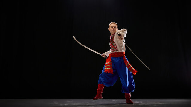 Ukrainian dancer, dancing Hopak with sabre pose, embodying artistry and strength in cultural dance performance against black background. Concept of traditions, folk style, art and history. Ad