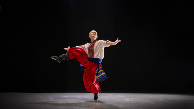 Male dancer in folk-style outfit performs elegant leap, arms extended, radiating confidence and joy, showcasing celebratory nature of Hopak. Concept of traditions, folk style, art and history. Ad