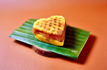 Heart shaped waffle cake on green banana leaf. Kue Bapel hati. Sweet dessert snack isolated on horizontal orange brown terracota background.