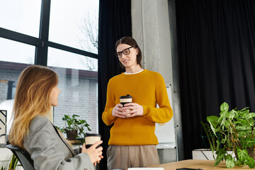 Two young individuals share ideas while enjoying coffee in a stylish office environment.