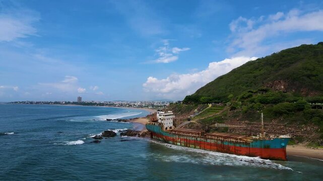 Aerial drone shot of the shipwreck near Vizag, offering a dramatic view of the rusted hull partially submerged in the ocean.