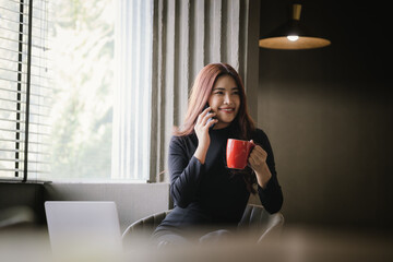 Fototapeta premium A confident young Chinese woman enjoys a peaceful coffee break in a modern cafe. Surrounded by city life, she relaxes with a book and portable device, balancing work, leisure, and indulgence.