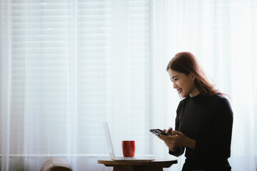 A young woman is relaxing in a cozy coffee shop, smiling as she sips her coffee. She uses her...