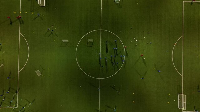 football training on an illuminated stadium in the evening. children and adults in jerseys run and exercise in circular training. small and large goals. view from above. the surroundings are dark