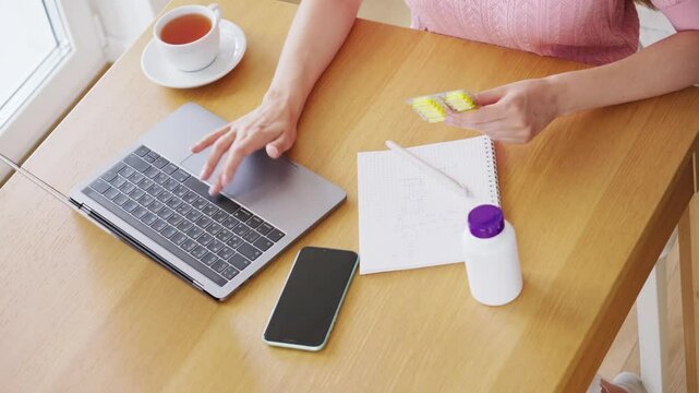 Young woman working with laptop computer in home kitchen. Work at home. Freelance, remote work. Omega-3. Food. Vitamins D, E, Fish oil in capsules