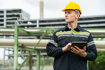 Refinery oil engineer worker in protection hardhat with digital tablet inspecting at petrochemical...