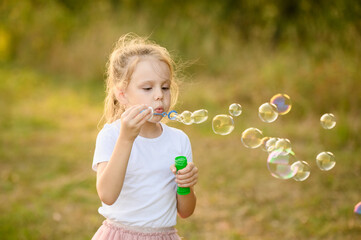 Cute girl blowing soap bubbles outside, having fun in nature in park on summer day. Happy childhood...