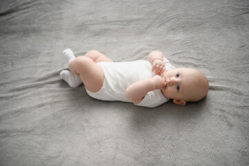Cute newborn baby lying on his back in crib, being active and sucking his thumb. Portrait of a...