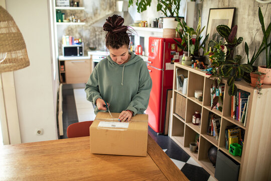 Woman opening package with scissors at home in cozy kitchen