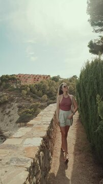 A young woman walking along a scenic stone path in Spain on a sunny day