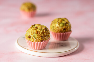  docinho de festa sabor pistache em uma forminha de papel rosa sob um pratinho de mármore e dois docinhos desfocados ao lado e atrás