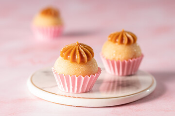 docinho de festa sabor churros em uma forminha de papel rosa sob um pratinho de mármore e dois docinhos desfocados ao lado e atrás
