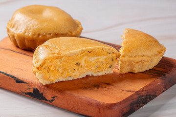 Torta pequena de frango aberta na frente e outra torta pequena fechada atrás sob uma tábua de madeira em uma mesa de madeira clara 