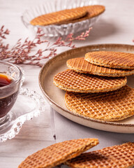 stroopwafel de caramelo sob um prato de caramica em uma mesa de madeira clara com uma xicara de café e uma flor seca rosa