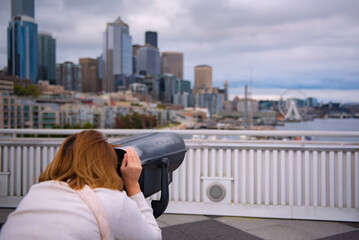 Rear view of woman looking over city through tourist telescope, Seattle, USA.