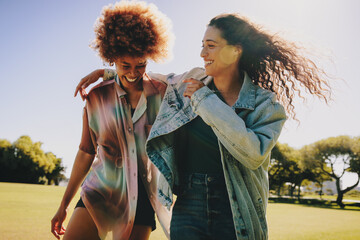 Joyful college girls having fun in a sunny urban park, sharing laughter and happiness on a bright...